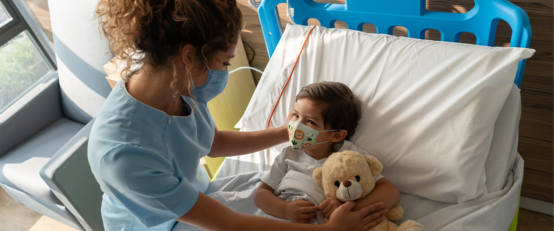 Female provider with boy holding teddy bear in hospital bed