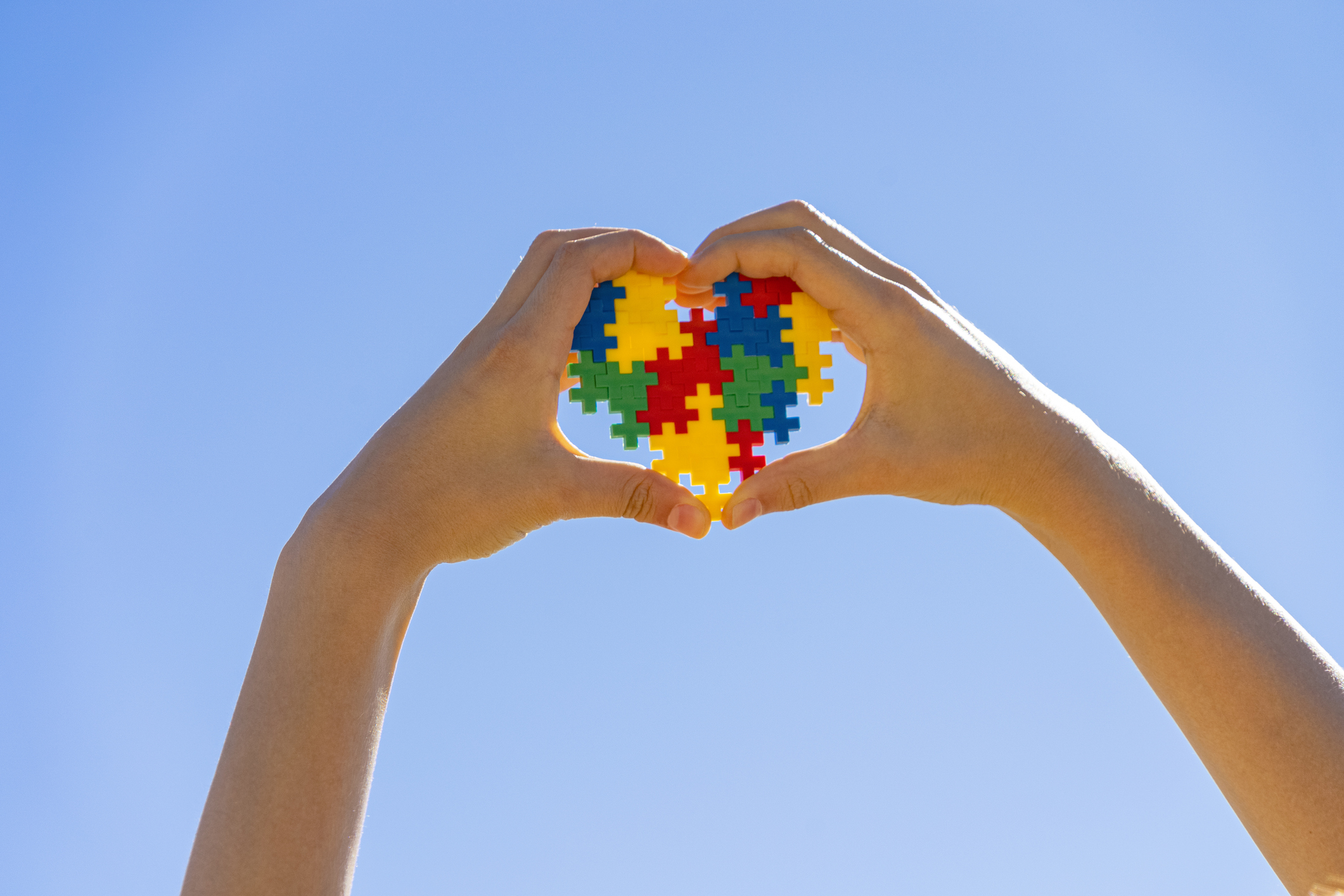 Child hand holding colorful heart on blue sky background. World autism awareness day concept