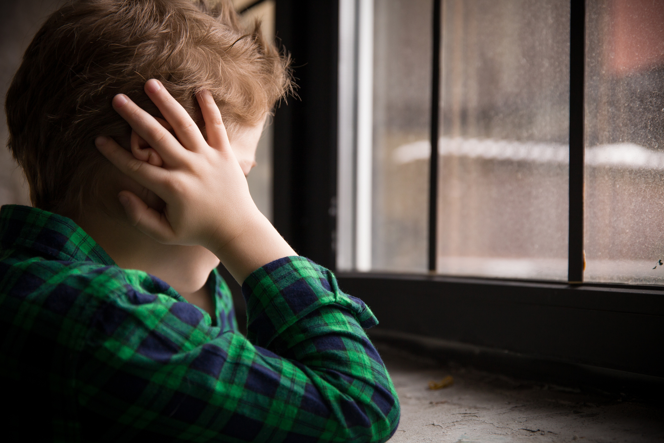 Boy with hands over ears looking out window