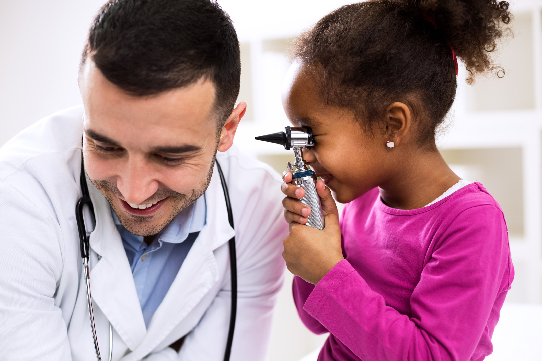 Young girl looking through otoscope into doctor's ear