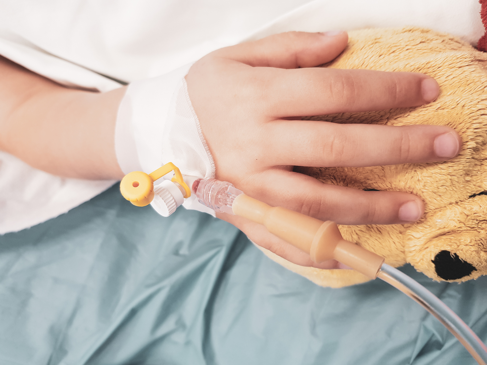 Hand of an ill little girl in a pediatric hospital reserve, with a cannula and holding a teddy bear