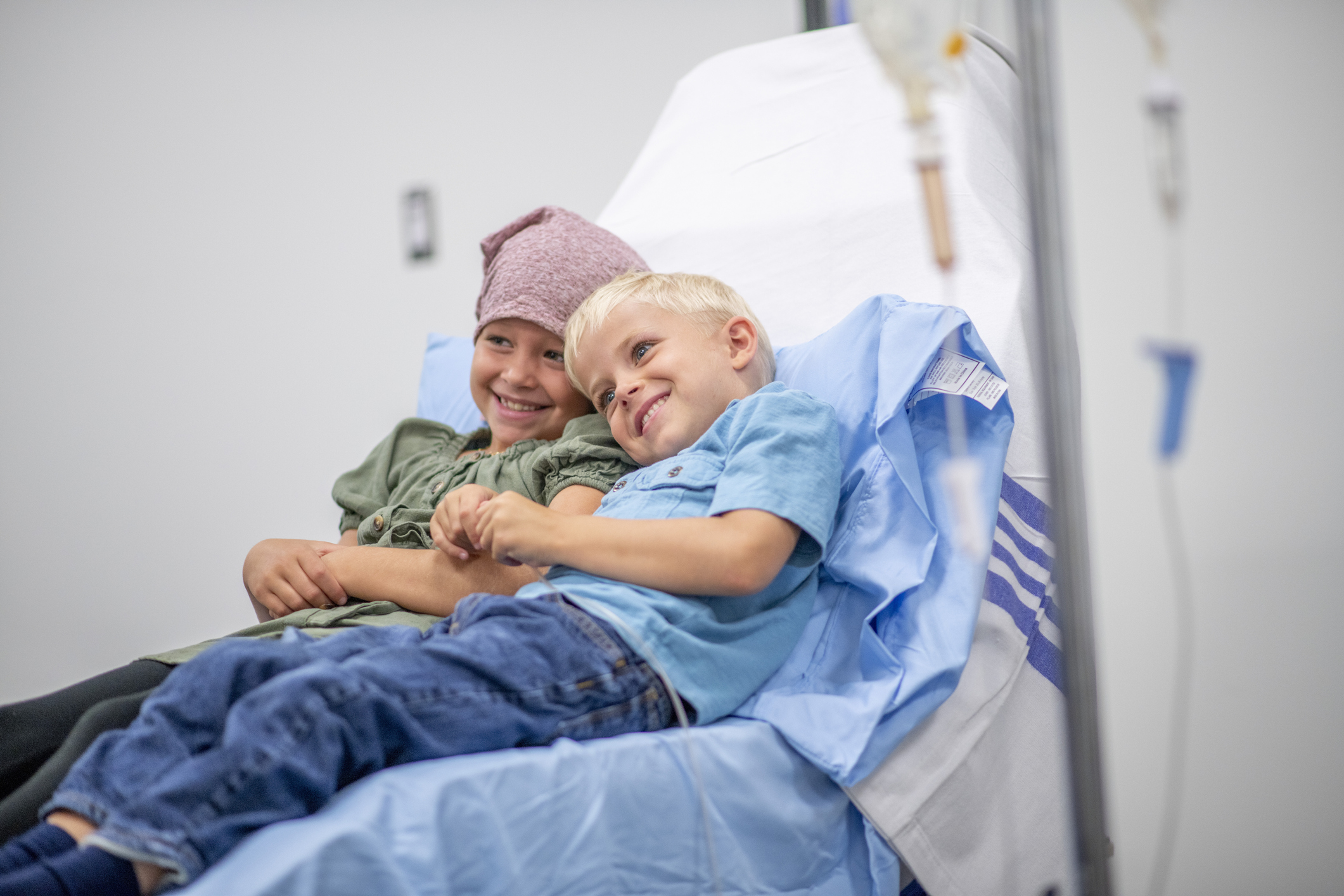 Young girl with bandana on head sitting with boy on hospital bed