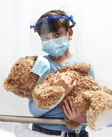Young boy holding teddy bear next to hospital bed