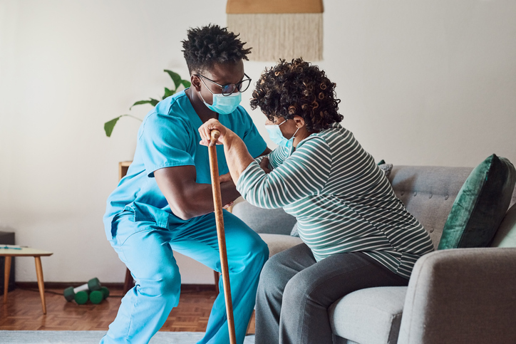a nurse helping a patient off of a sofa