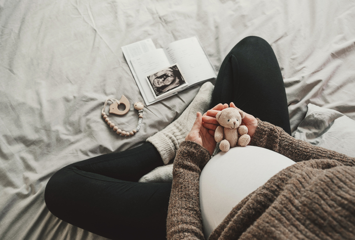 a pregnant woman sitting on the bed with baby toys