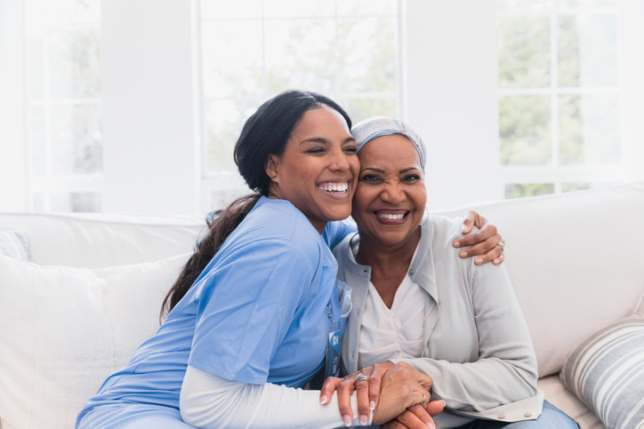 a nurse and patient sitting on a sofa smiling