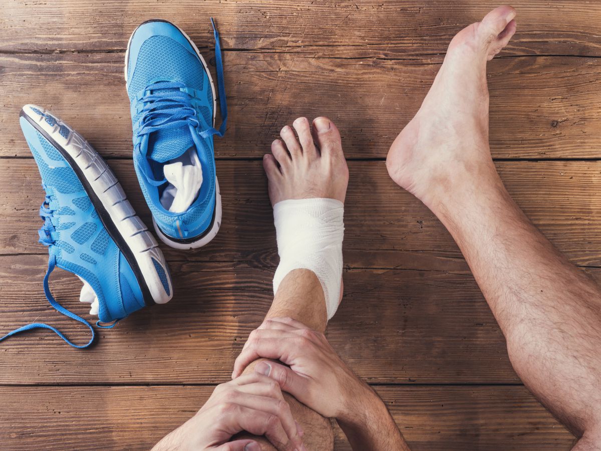 man with bandaged left foot sits on hardwood floor next to his running shoes