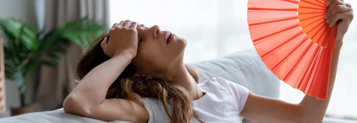 woman on couch fanning herself indicating hot flashes due to menopause