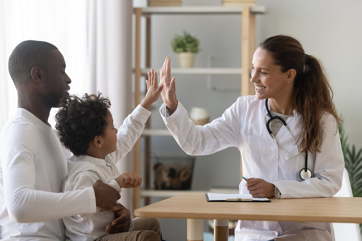 Young boy on man's lap giving high five to female doctor