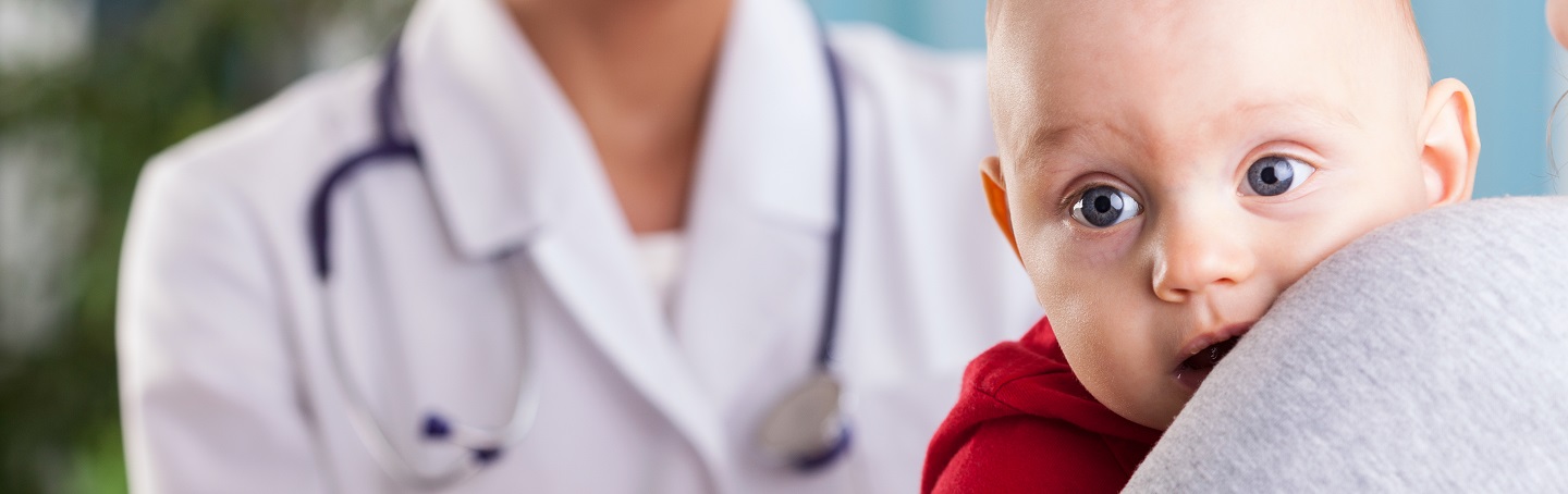 closeup of baby being held by parent with pediatrician in background