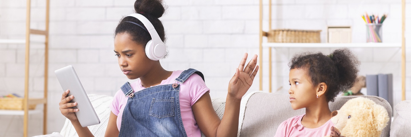 stock photo of adolescent with headphones waving little sister away indicating puberty moodiness