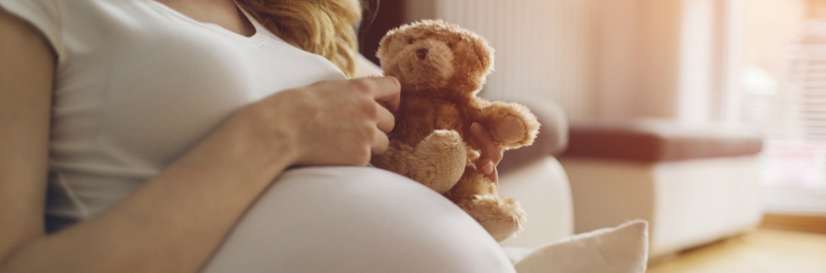 closeup of pregnant woman holding teddy bear on her belly