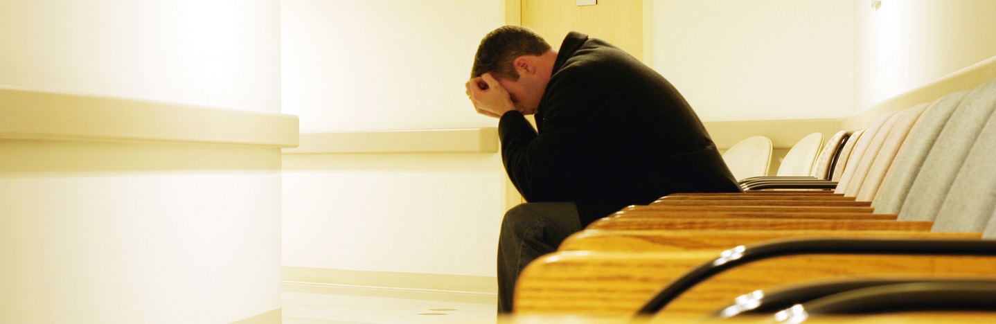 stock image of dejected man with head in hands in hospital hallway