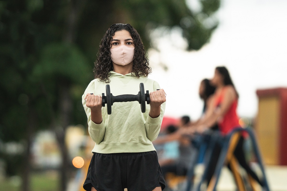 stock image of teen girl wearing mask and holding dumbbell up to camera image
