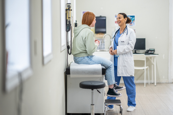 teen girl sitting on exam table talking to female doctor