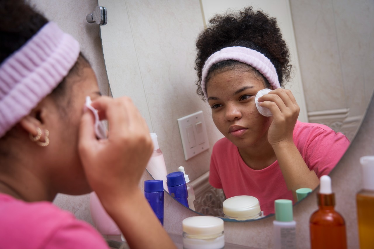 A teen girl applies skincare in a mirror