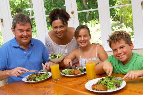 A family of parents and two kids eats a heart-healthy meal of lean protein, salad and fresh fruit juice together.