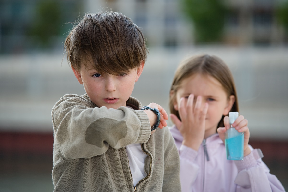 stock photo of a child coughing into his elbow and another using hand sanitizer