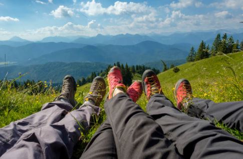 A widescreen view of 3 sets of feet wearing hiking sneakers, with a mountain line on the horizon.